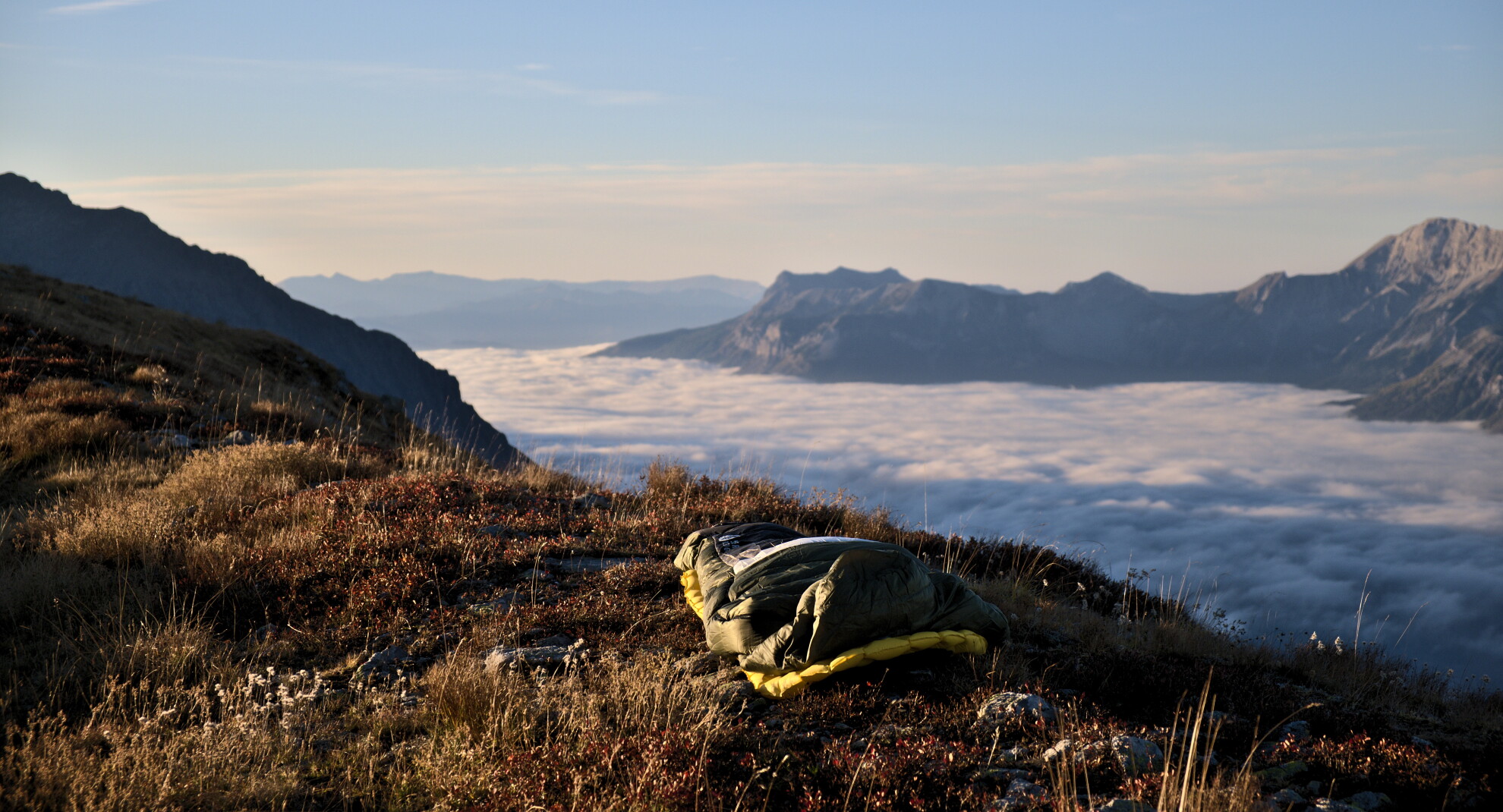 Schlafsack auf einem Grasrücken über einem Wolkenmeer